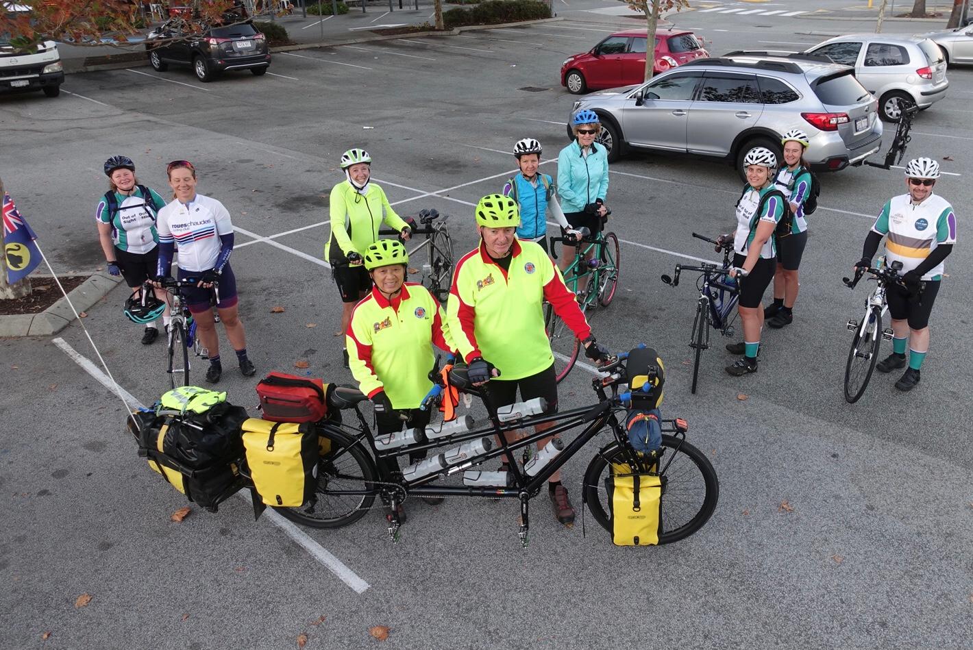 WATCAC riders on four tandems and one single bike are standing with Bas and Nga’s as they prepare to mount their touring tandem, loaded with front and rear panniers plus a ‘Bob’ style trailer flying a WA state flag. 