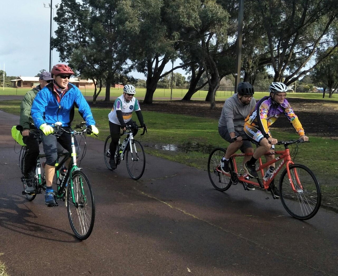 Two tandems and a single bike are riding along a shared path in the George Burnett Reserve.