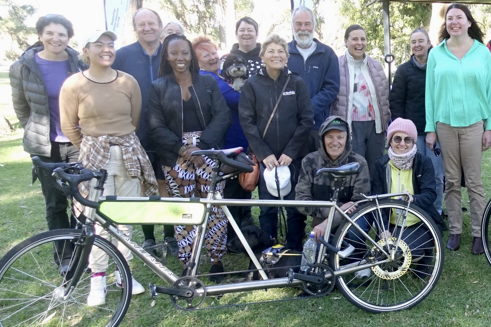 Group photo in front of a silver tandem, including volunteers involved in fundraising, tandem clinics and our general riding programs.