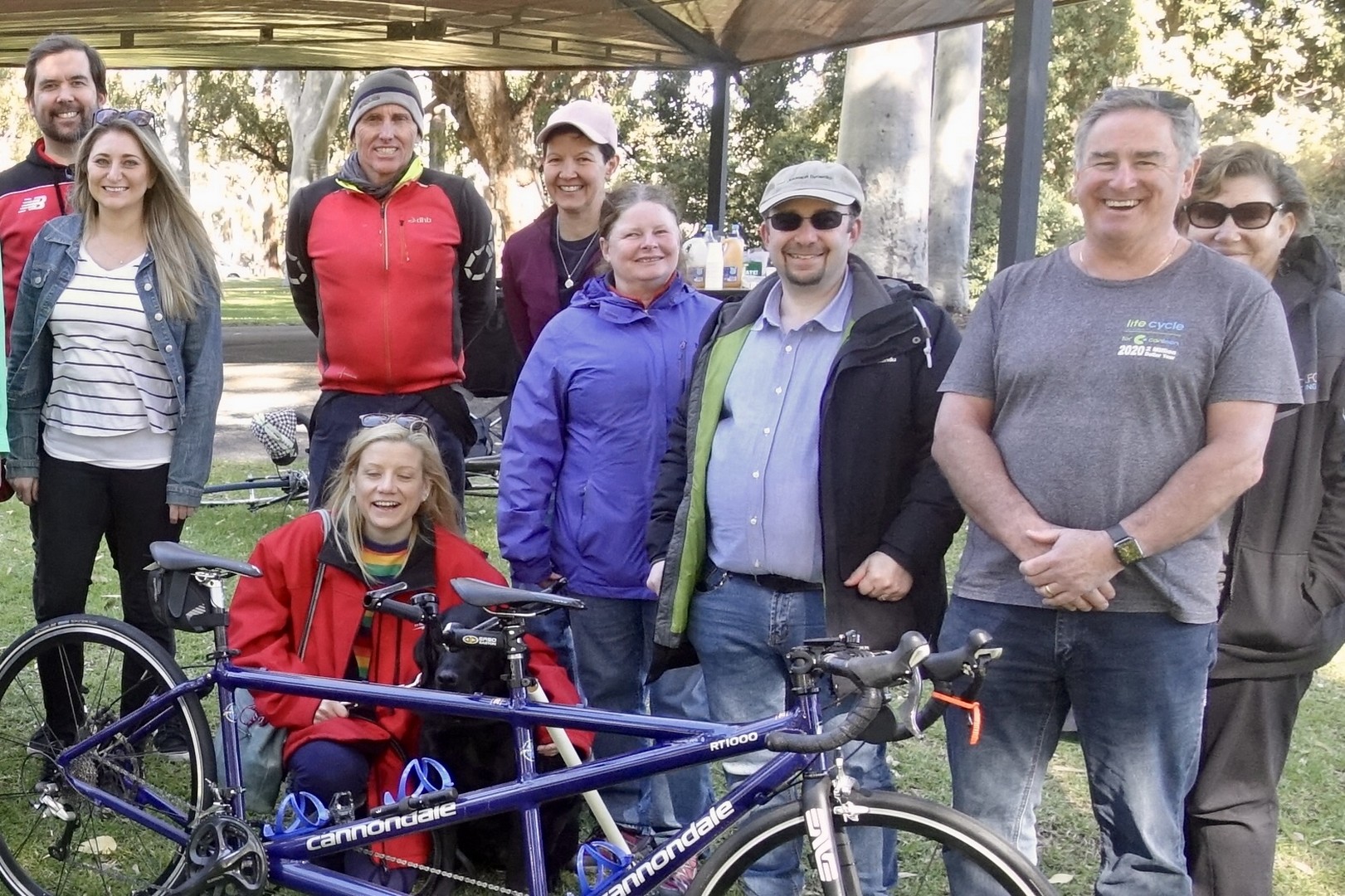 Another group photo in front of a blue tandem, including many of our volunteers involved in fundraising, tandem clinics and our general riding programs.